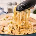 Closeup of tongs pulling up strands of fettuccine Alfredo.