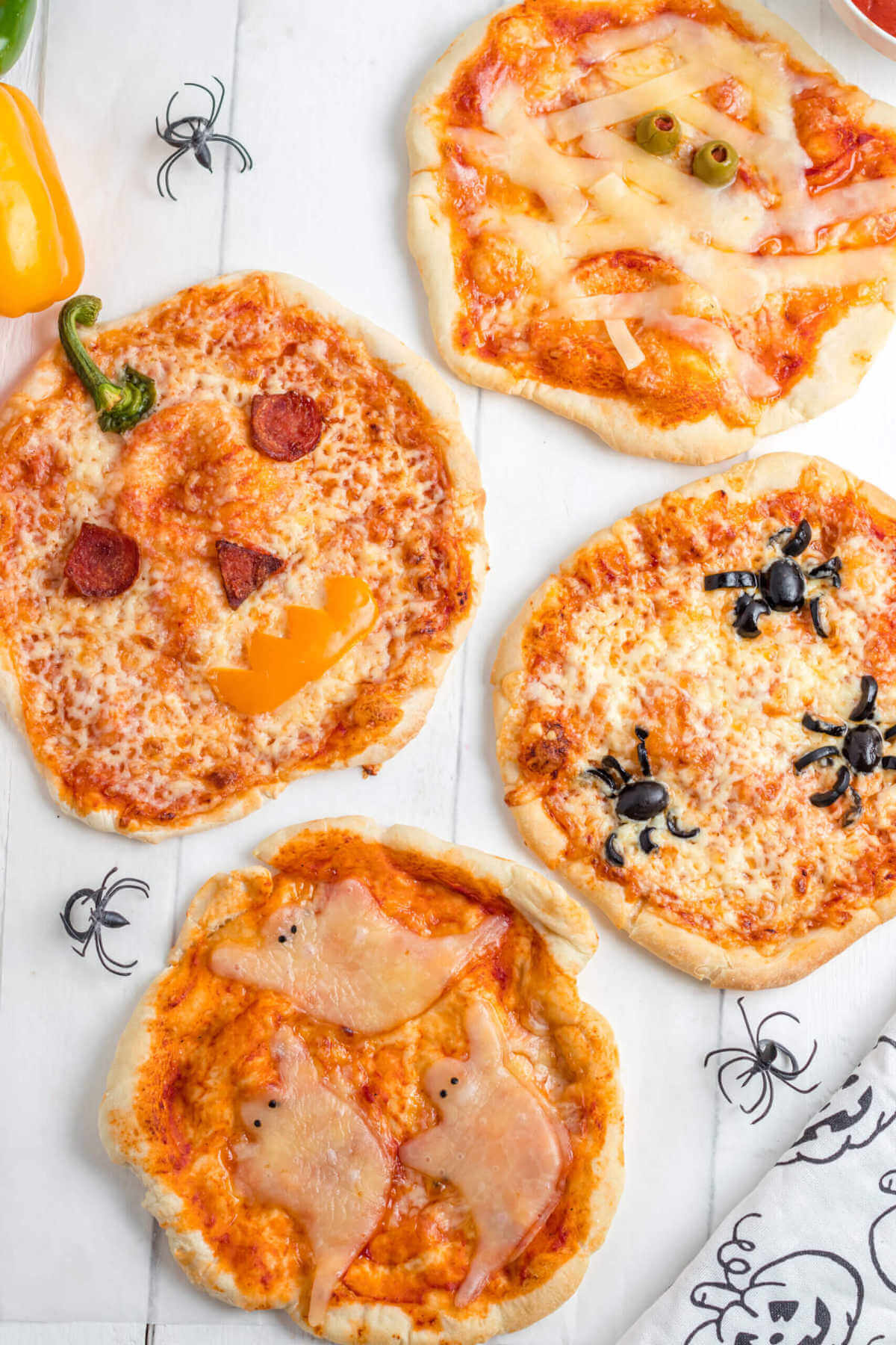 Four pizzas decorated with Halloween characters of ghosts, jack-0-lantern, spiders, and mummies. 