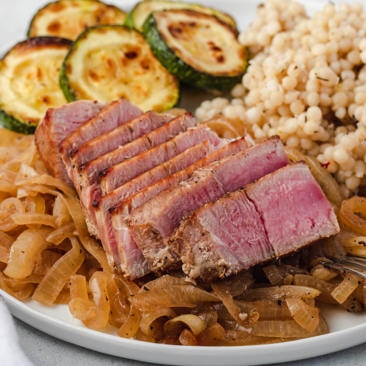Sliced fresh yellowfin on a plate with onions, zucchini , and couscous.