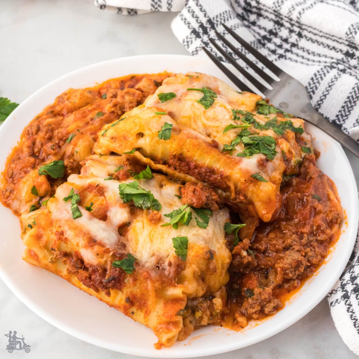 Two Lasagna Roll Ups on a white plate served with a tomato ragù sauce.