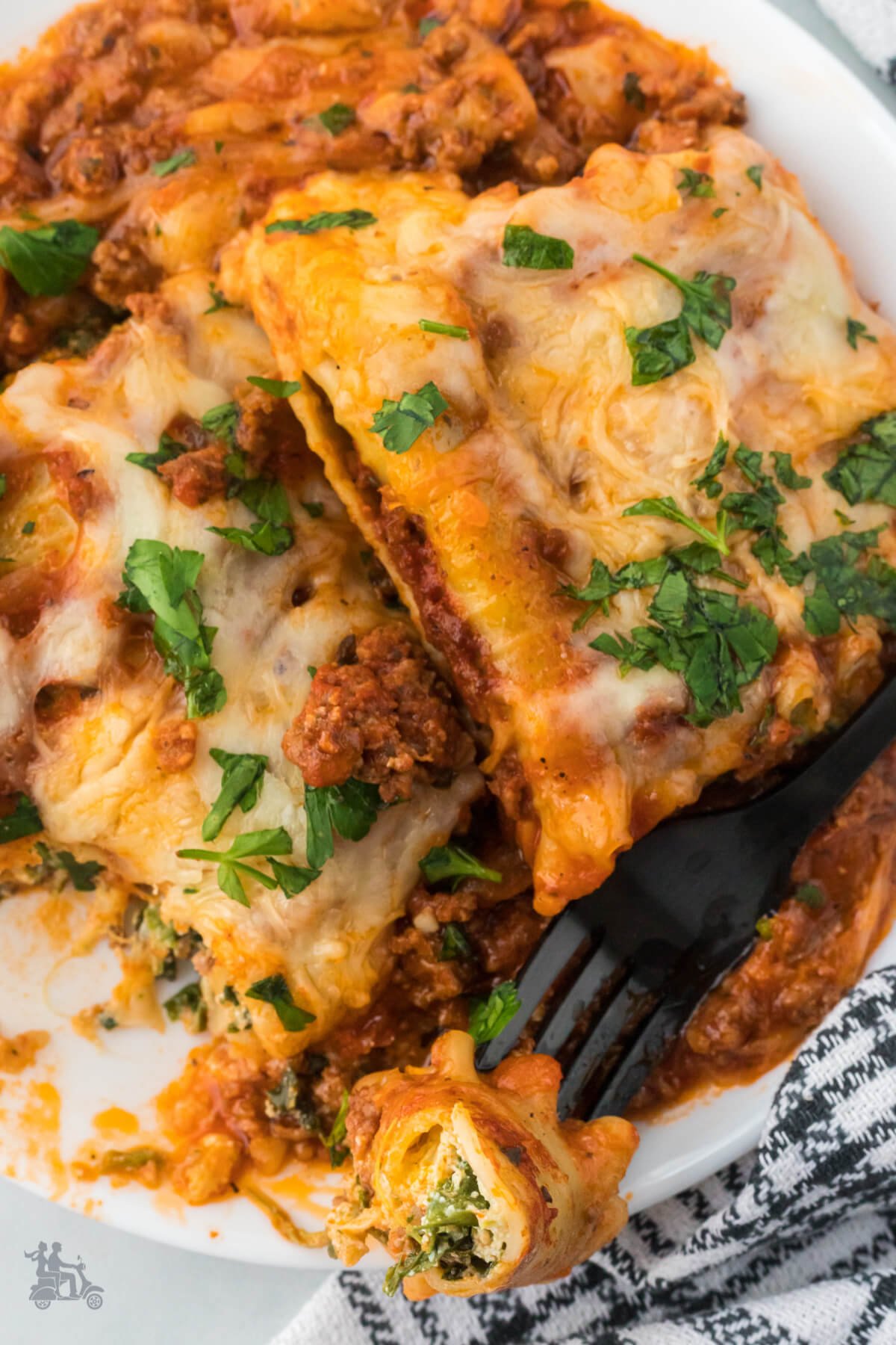 Close up of a Lasagna roll up covered in meat sauce and garnished with Italian parsley. 