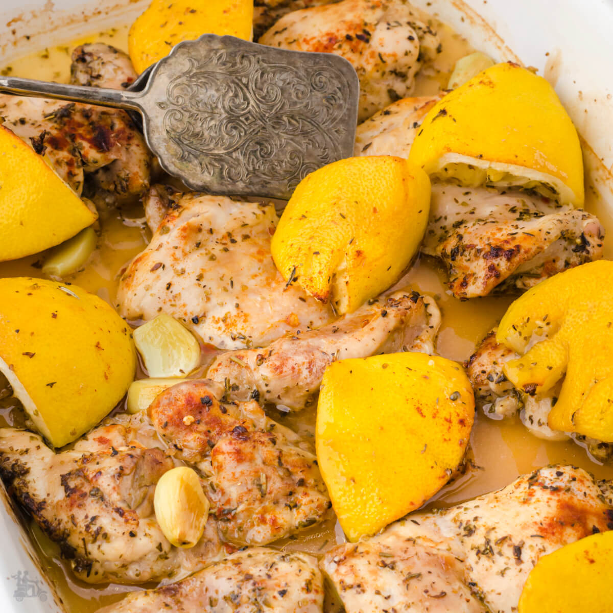 Close up of Garlic Lemon Chicken Thighs in a casserole dish with a serving spoon.