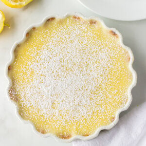 A white tart pan filled with a lemon curd filling and sprinkled with powdered sugar.