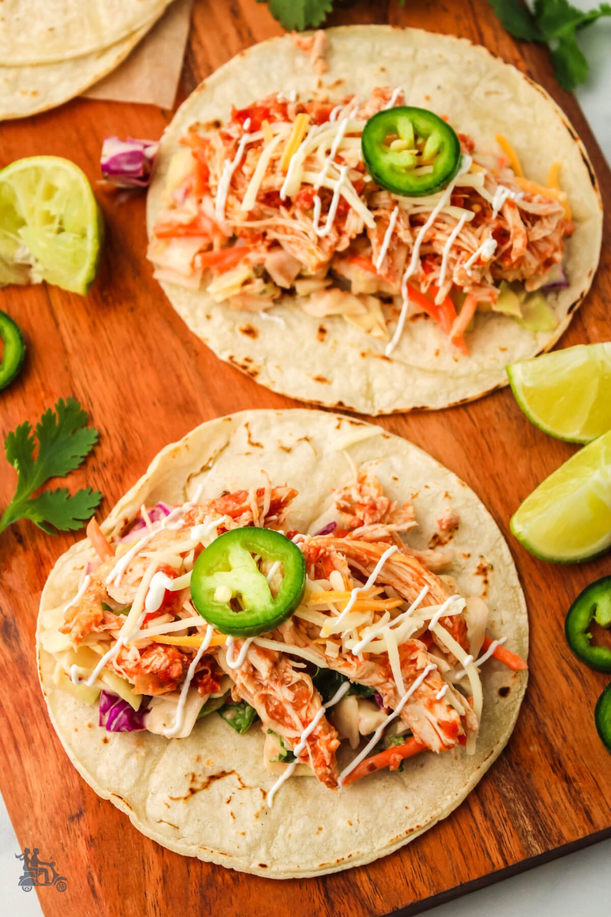 Two Shredded Chicken Tacos on a cutting board with lime and cilantro on the side. 
