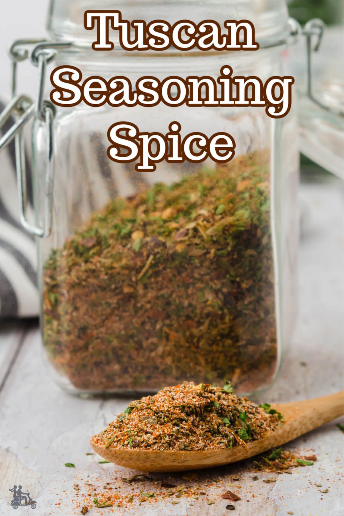 A jar and a wooden spoon with Tuscan Seasoning spice blend. 