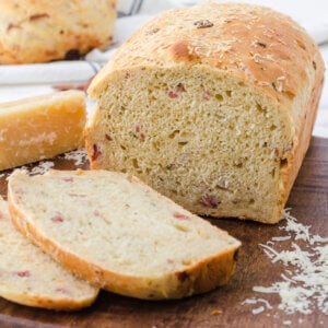 Loaf of golden brown pizza bread sliced on a cutting board with specks of salami and herbs studding the loaf and slice.