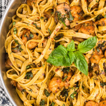 Skillet filled with fettuccine pasta, shrimp, mushrooms and a basil sprig on top.