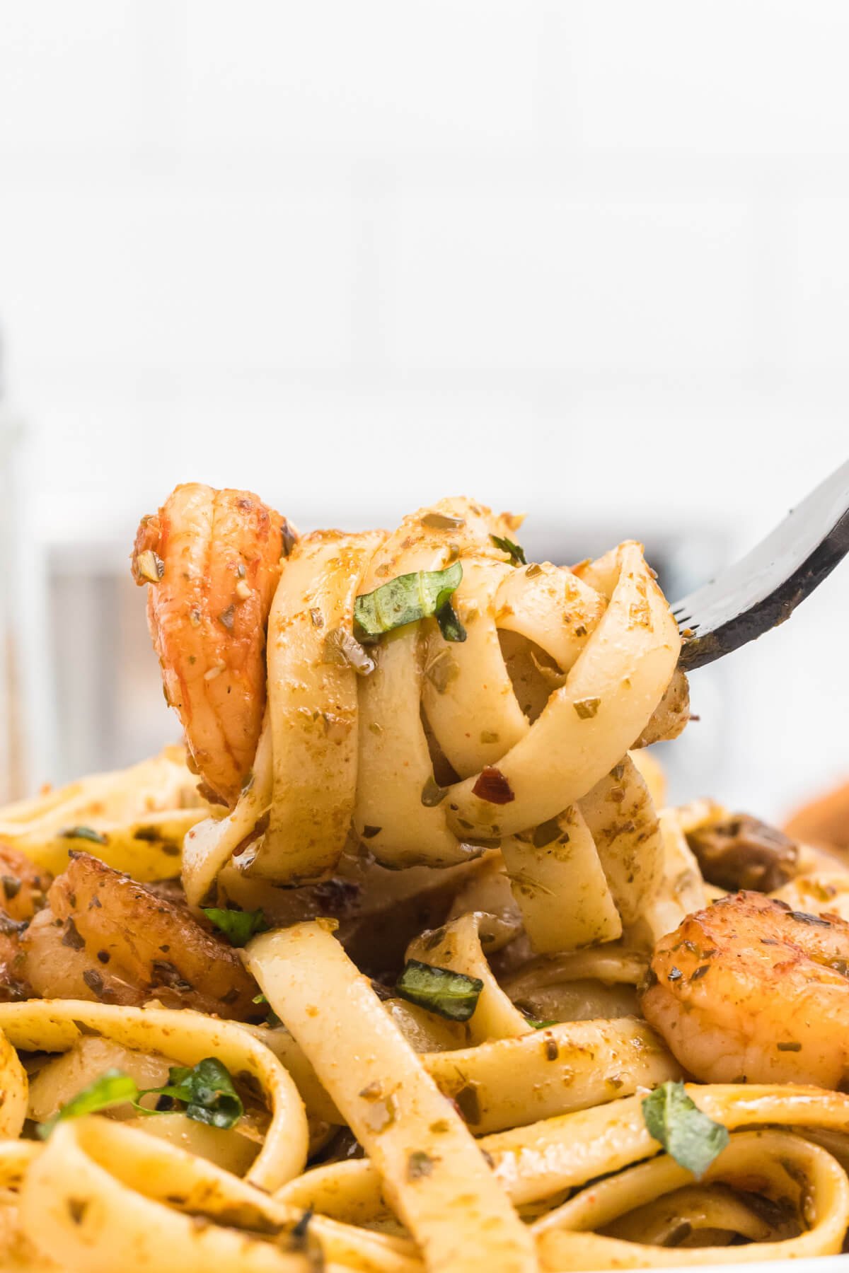 A closeup of a fork holding a bite of shrimp with fettuccine and mushrooms. 