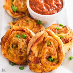 Pizza pinwheels surround a white bowl of marinara dipping sauce.