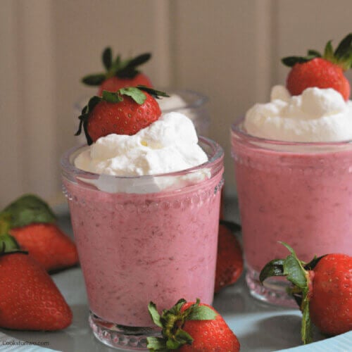 Two glasses filled with strawberry mousse topped with whipped cream and strawberry.
