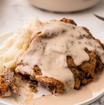 Chicken fried steak covered with Milk gravy on a white plate.
