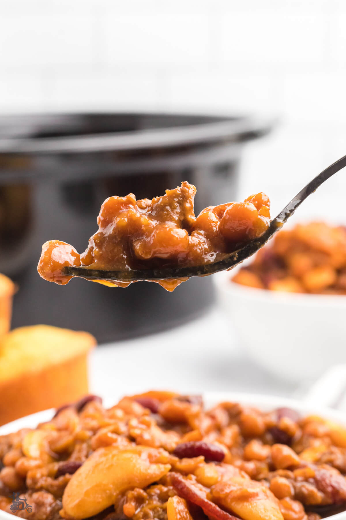 A spoonful of Slow cooker baked beans with the crockpot in the background. 