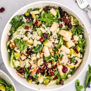 Overhead view of large white bowl filled with arugula salad tossed with pears, gorgonzola cheese, cranberries, and walnuts.