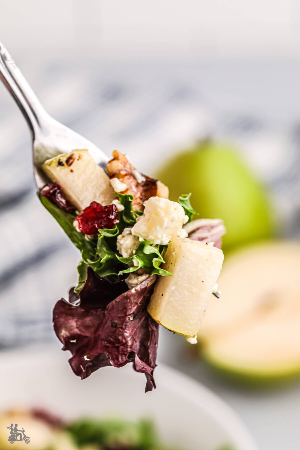 A fork holding a bite of Arugula Salad with Pears , cheese, and cranberries. 