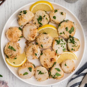A plate filled with sautéed scallops on a white plate with lemon wedges