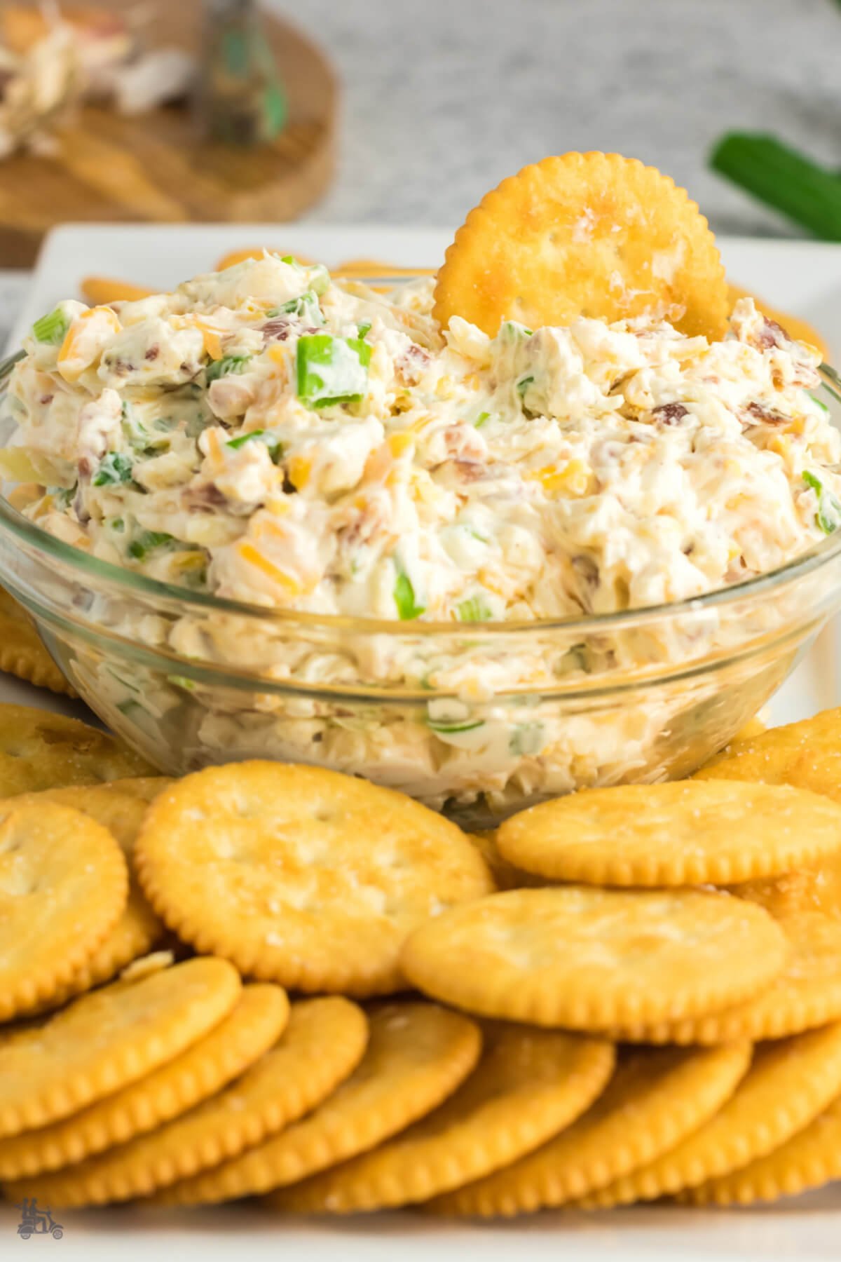 A side view of a glass bowl of cream cheese dip appetizer with Ritz crackers. 