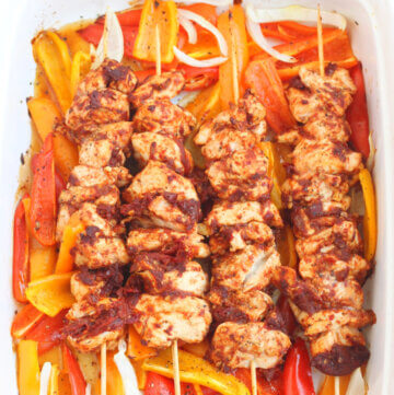 Chicken Kebab Skewers on a bed of onion and colored peppers.