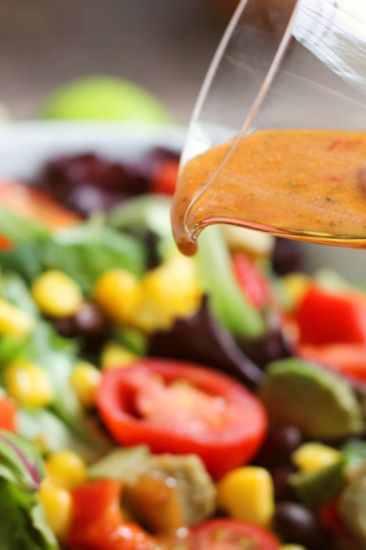Closeup of the Copycat Chipotle Mexican Grill's Honey Vinaigrette pouring over a tossed salad.