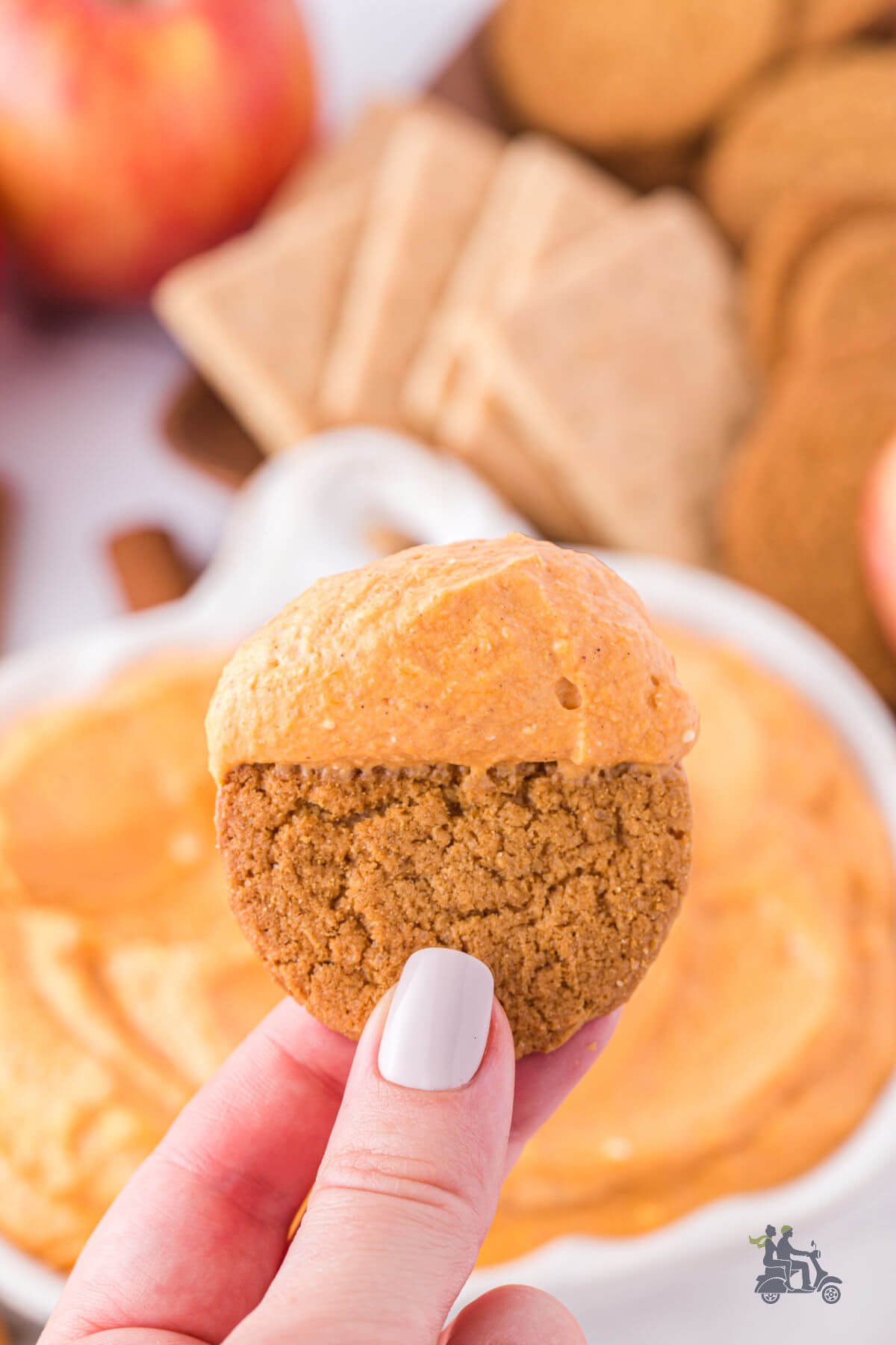 Hand holding a ginger snap that's been dunked in the pumpkin dip with cream cheese. 