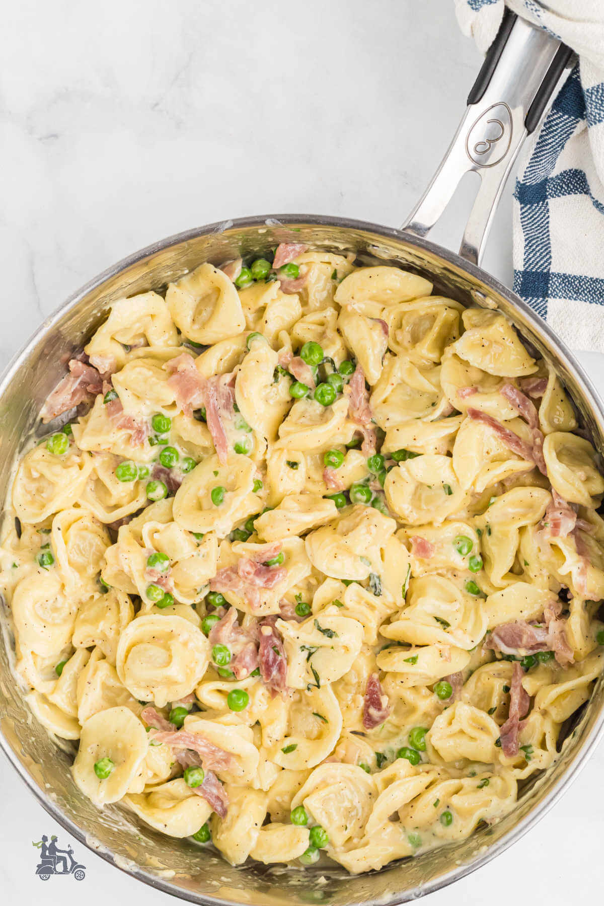 A deep skillet filled with tortellini alla Panna with prosciutto and peas. 