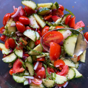 A bowl filled with tomatoes, basil, cucumbers and a spoon.