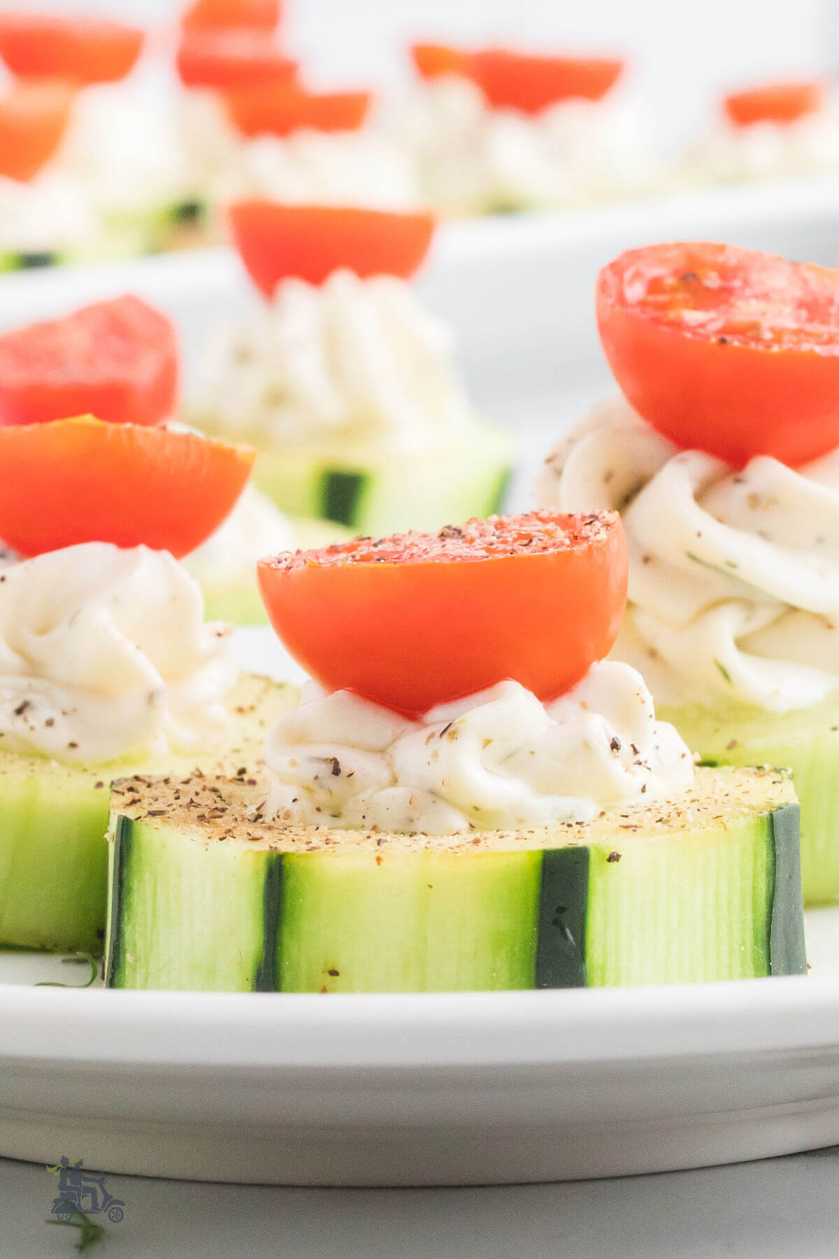 Closeup of cucumber appetizer bites with cream cheese and tomato hlaves. 