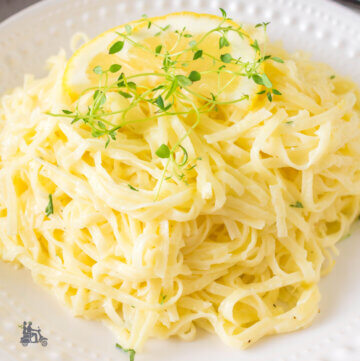 Pasta al Limone recipe serving on a white plate with lemon slice and fresh thyme leaves on top.