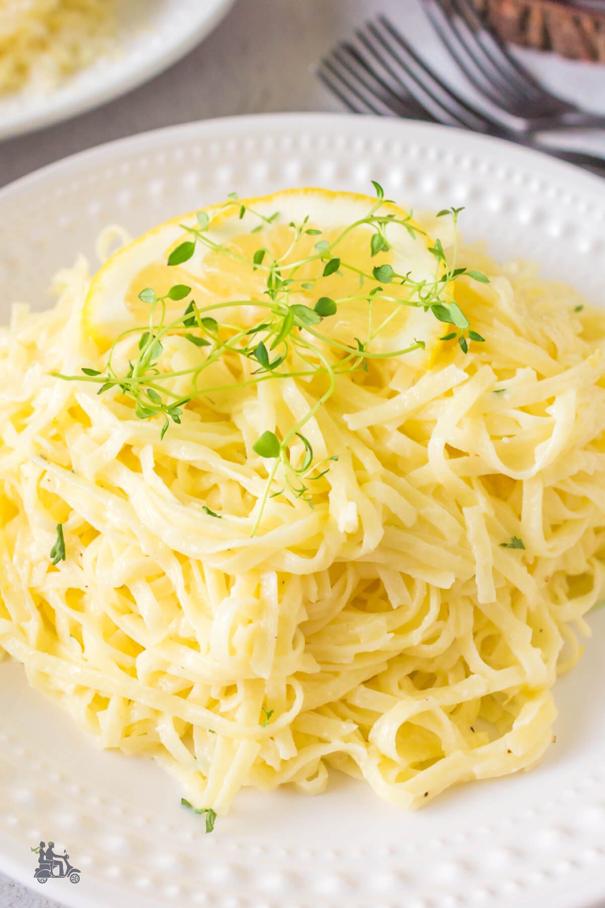A serving of thin tagliolini pasta al limone on a white plate with sprinkle of fresh thyme. 