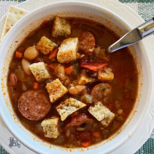 15 Bean Soup with Kielbasa sausage slices in a white soup bowl topped with homemade croutons.