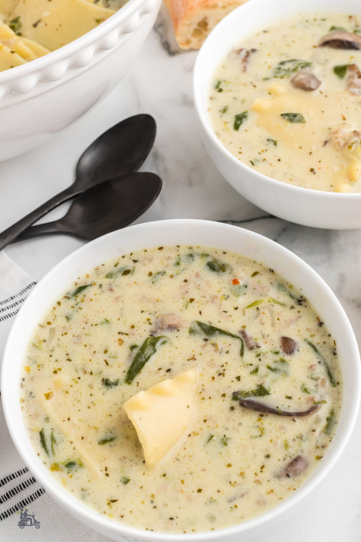 Two white soup bowls filled with a creamy white lasagna soup.