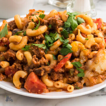 A white plate filled with Johnny Marzetti casserole with a sprinkle of parsley on top.
