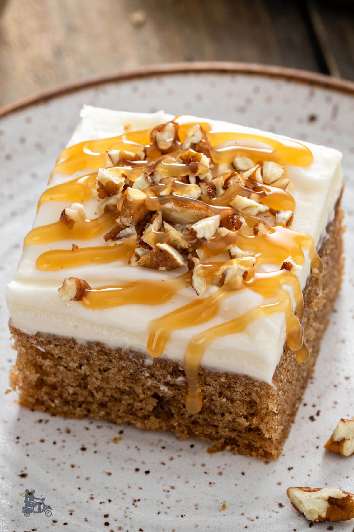 Serving square of spice cake with cream cheese topping sprinkled with walnuts and drizzled with caramel sauce. 