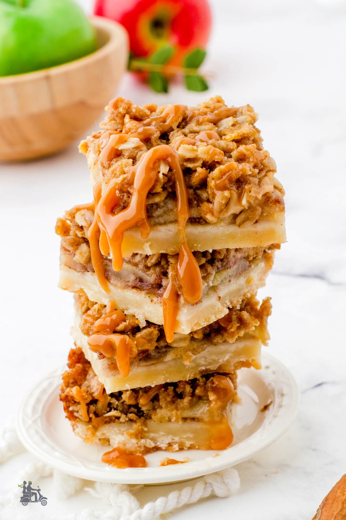 Salted caramel apple pie bars stacked up on a white plate with caramel drizzle running down the side. 