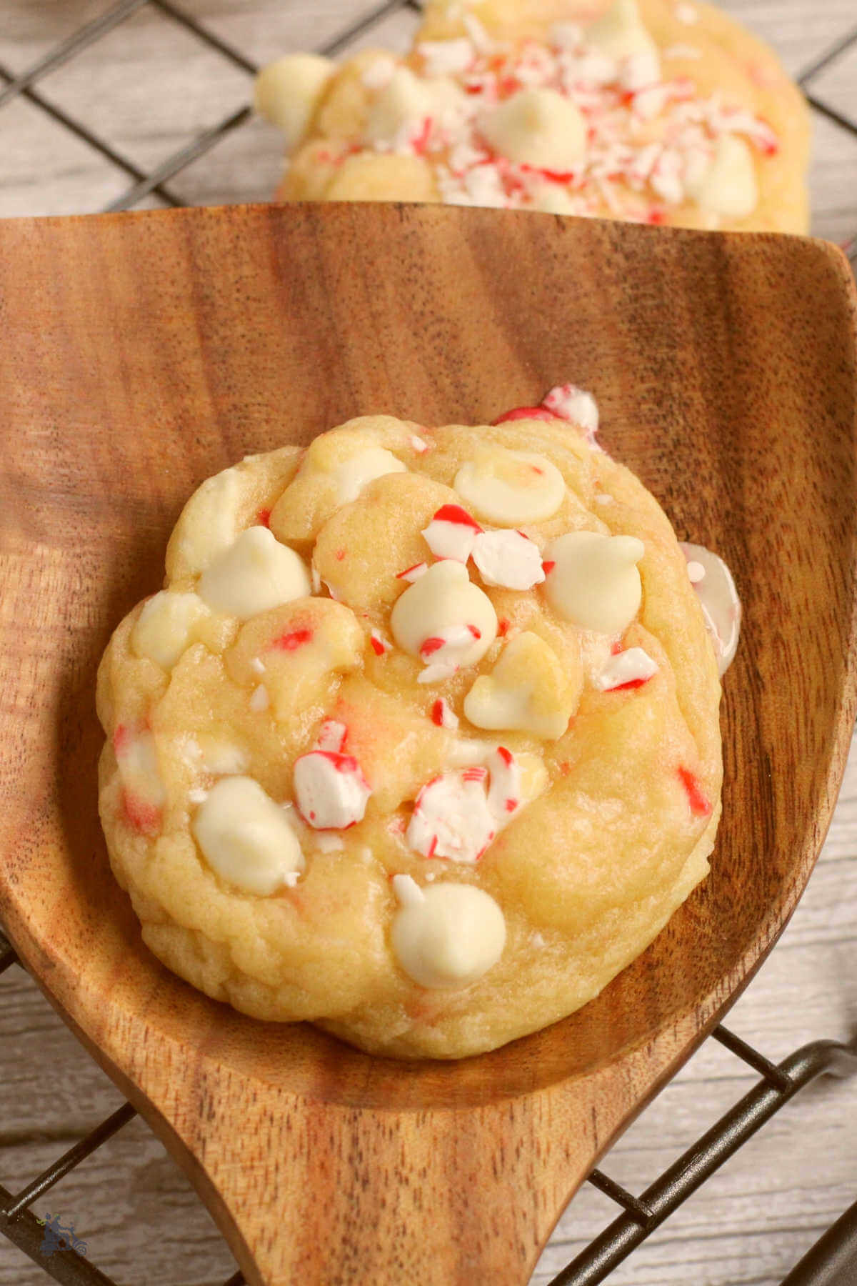 A wooden spatula holding a Peppermint White Chocolate Chip Christmas cookie with crushed candy canes on top. 