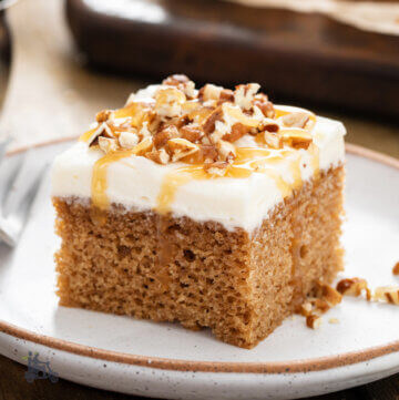 Pumpkin Spice Cake with Cream Cheese Frosting frosting sprinkled with walnut pieces on a ceramic plate with fork.