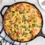 A cast iron skillet holding the Beefy Ravioli Bake with torn basil leaves sprinkled on top.