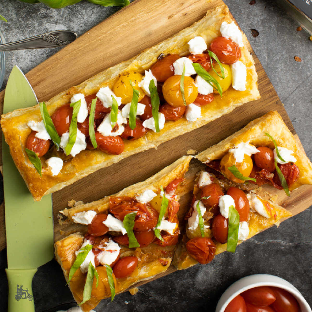 Two bruschetta pizzas made with puff pastry dough and topped with roasted tomatoes and goat cheese with julienned basil.
