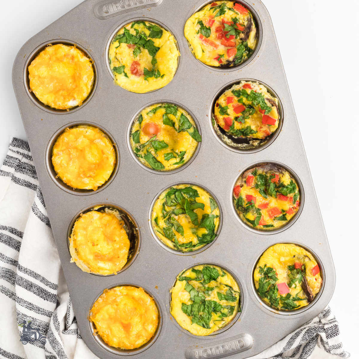 Muffin pan filled with 3 different types of egg muffins including ones with spinach, bacon, red bell pepper and cheese.
