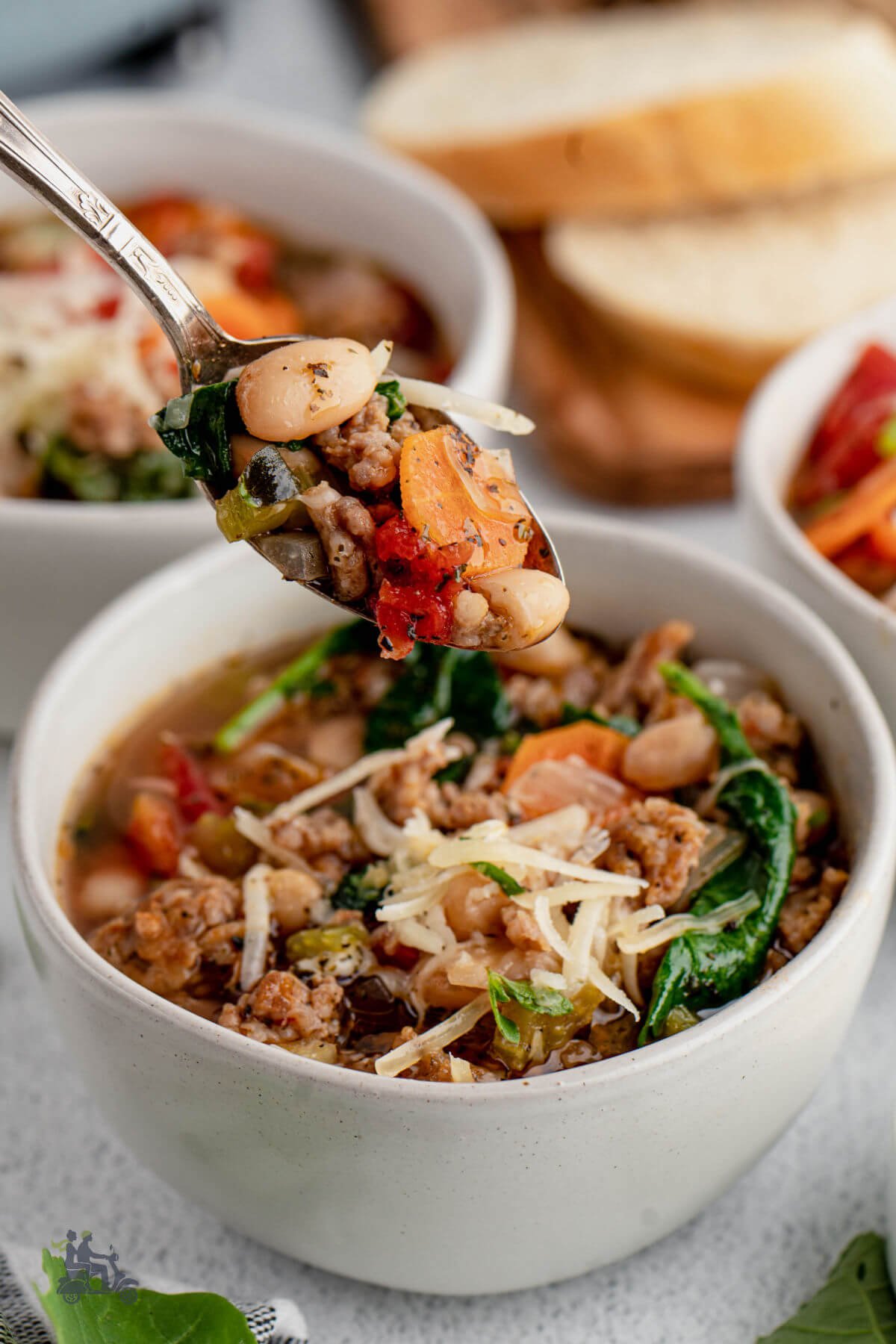 A spoon holding some of the white bean soup with sausage, kale, and tomatoes. 