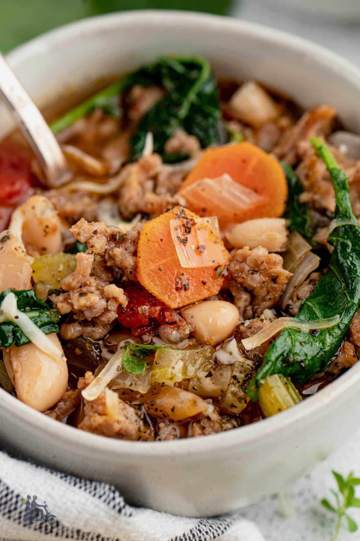 A white bowl filled with Italian White Bean Soup with Sausage and Kale and a spoon in the center. 