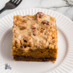 A serving square of pumpkin coffee cake topped with a pecan streusel with a sweet glaze over the top.