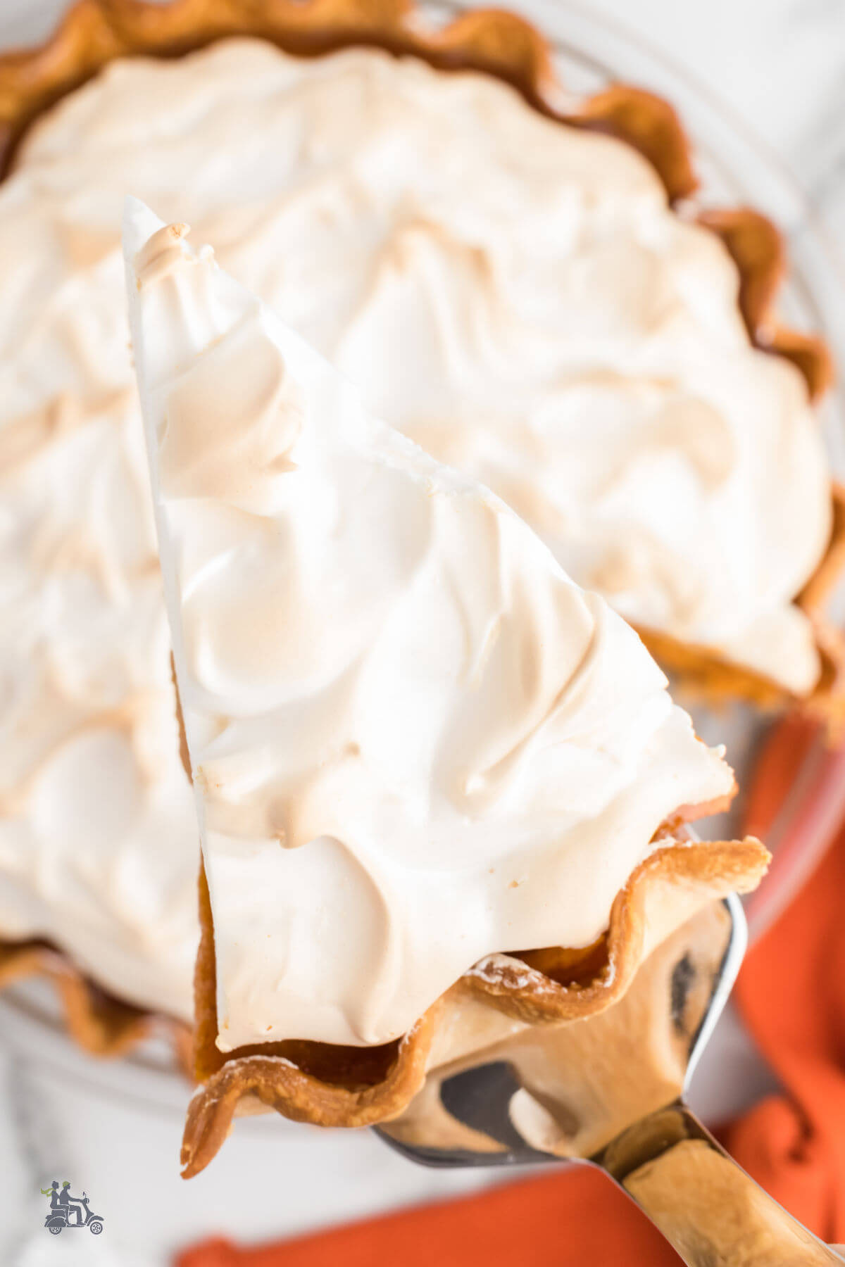 A sweet potato pie topped with marshmallow meringue with a spatula holding a wedge. 