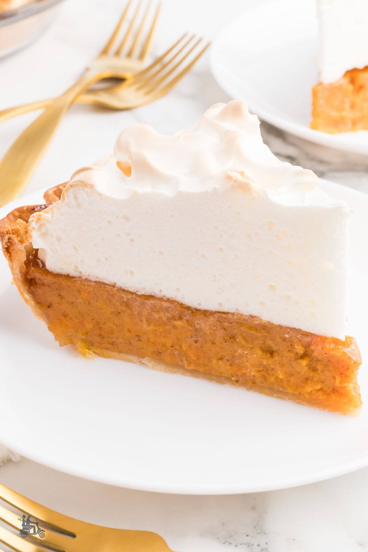 Sweet potato pie with a marshmallow meringue topping on a white plate with gold forks in the background. 