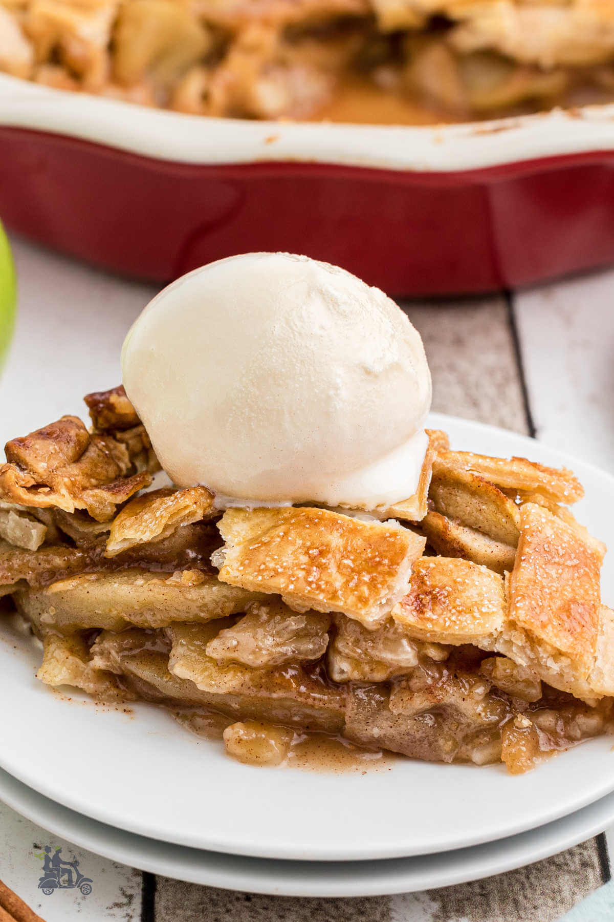 A piece of a latticed top wedge of apple pie with a scoop of vanilla ice cream on top. 