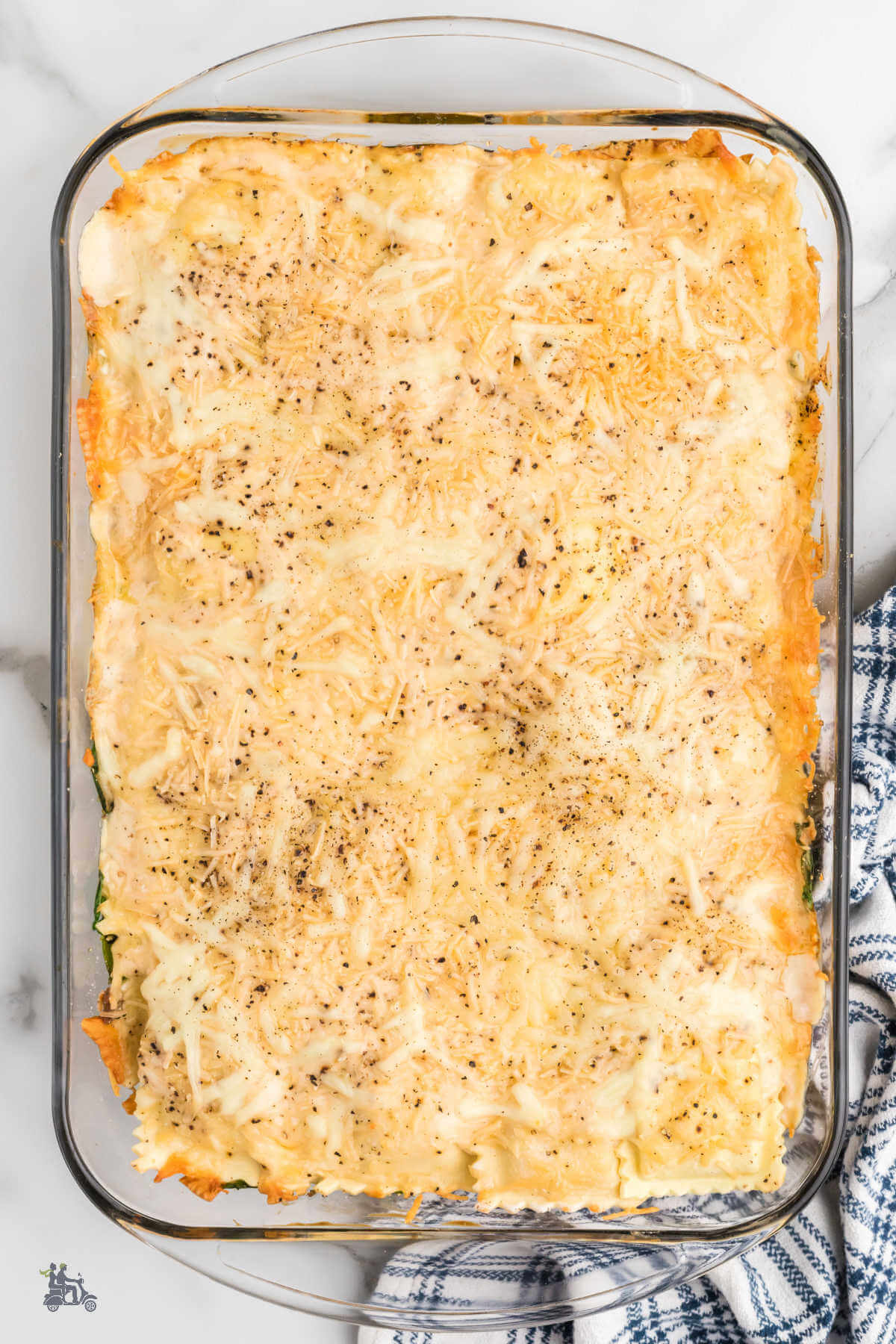 A glass casserole dish with baked white lasagna made with cheese ravioli and layered with spinach, sausage, and Alfredo sauce.