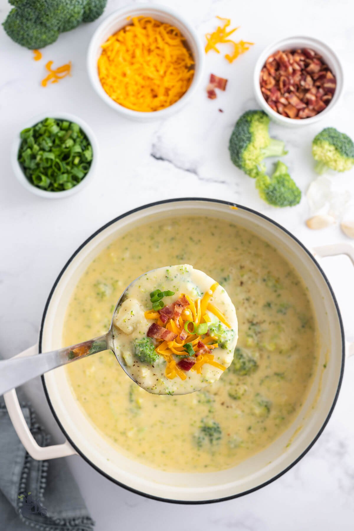 A Dutch Oven filled with Broccoli Potato Soup with a ladle filled with it. 