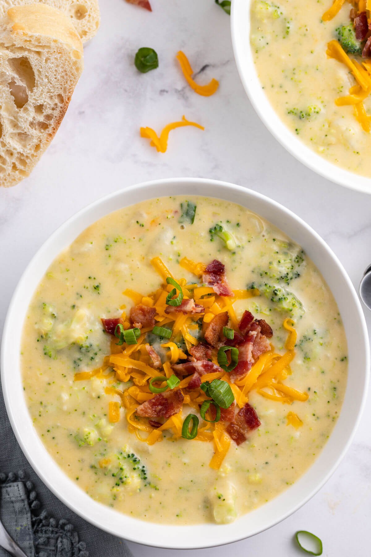 A big bowl of creamy cheddar potato broccoli soup topped with bacon pieces, shredded cheddar, and green onions. 