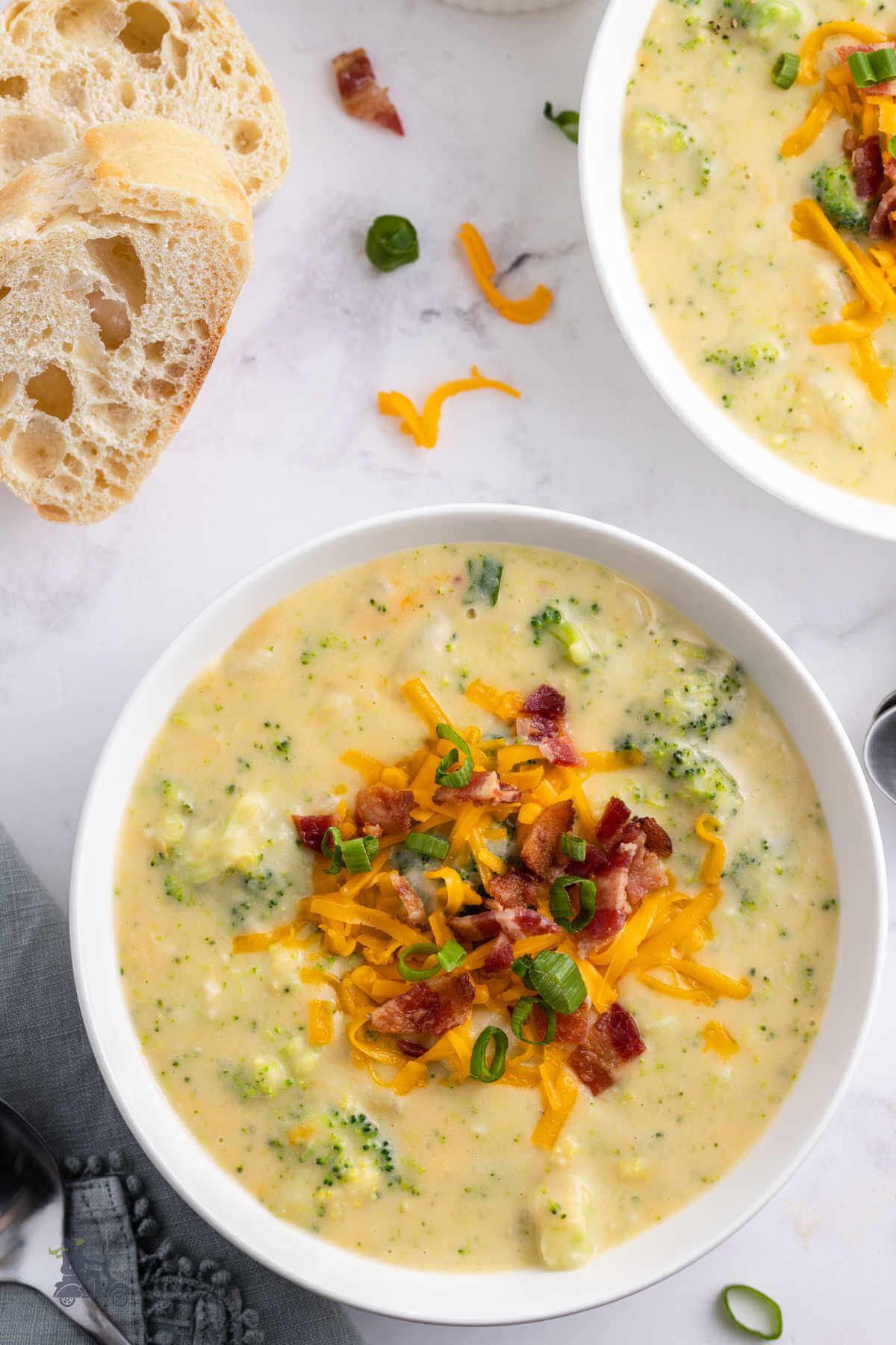 Overhead view of two bowls of broccoli potato soup garnished with cheddar cheese, bacon bits, and green onion. 