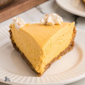 A slice of no bake pumpkin pie with whipped cream florets on top and a gingersnap crust.