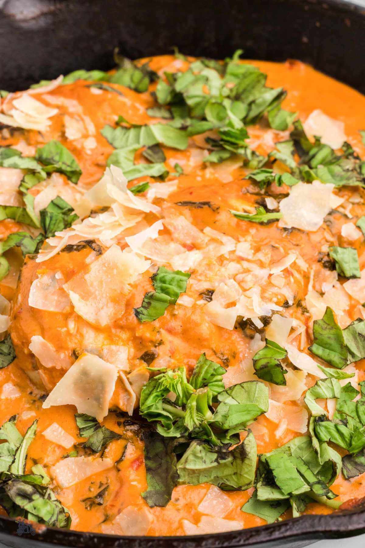 Close up of skillet chicken with creamy tomato kale sauce topped with fresh basil and shaved parmesan cheese. 